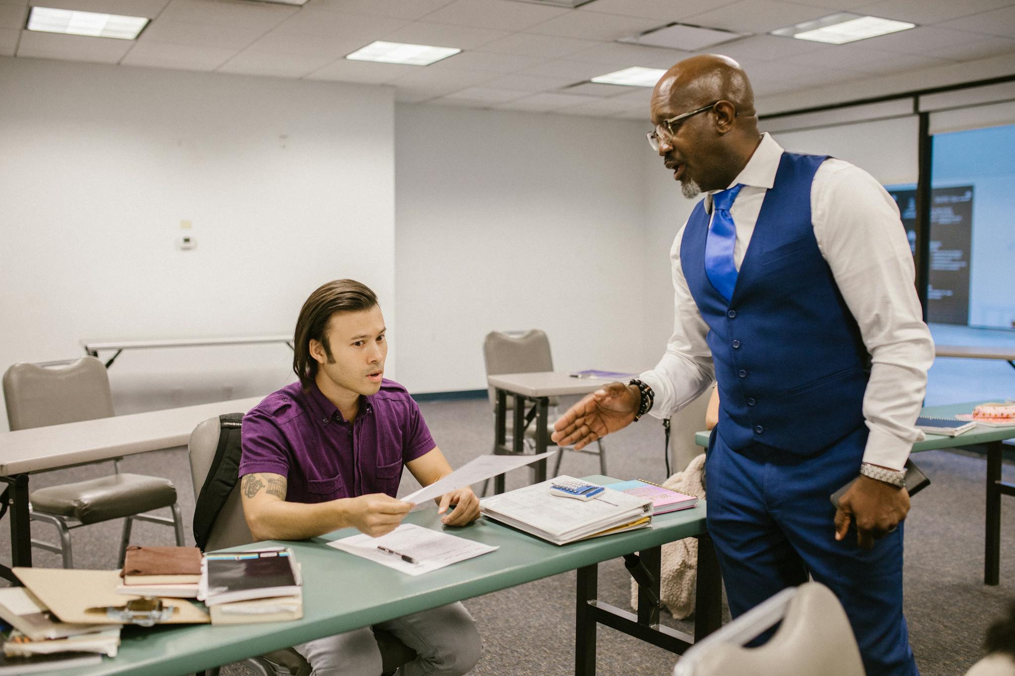 A teacher and student engaged in a discussion over an exam paper in a classroom setting.